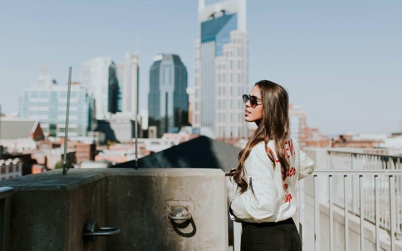 woman with sunglasses stands on a rooftop overlooking the city